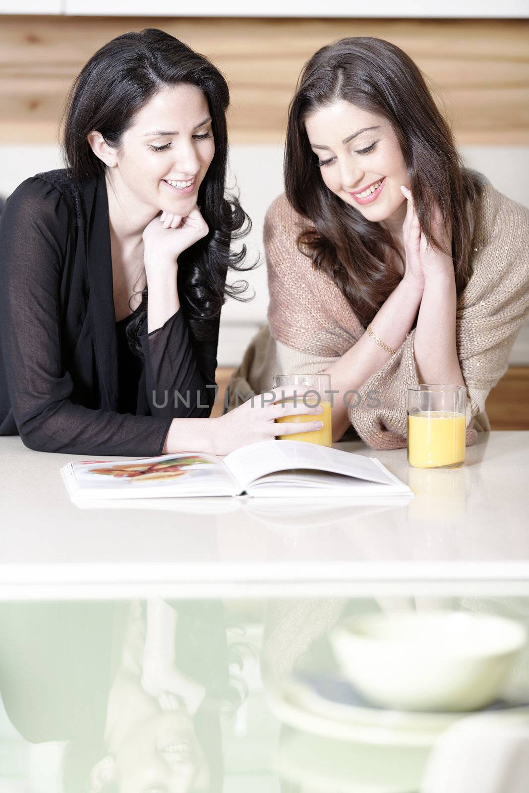 Two attractive young women reading from a cookery book in a kitchen