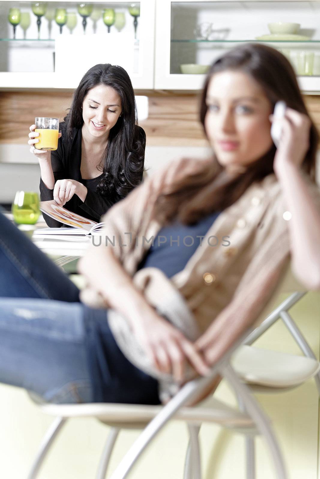 Two friends in a kitchen relaxing on the phone and reading