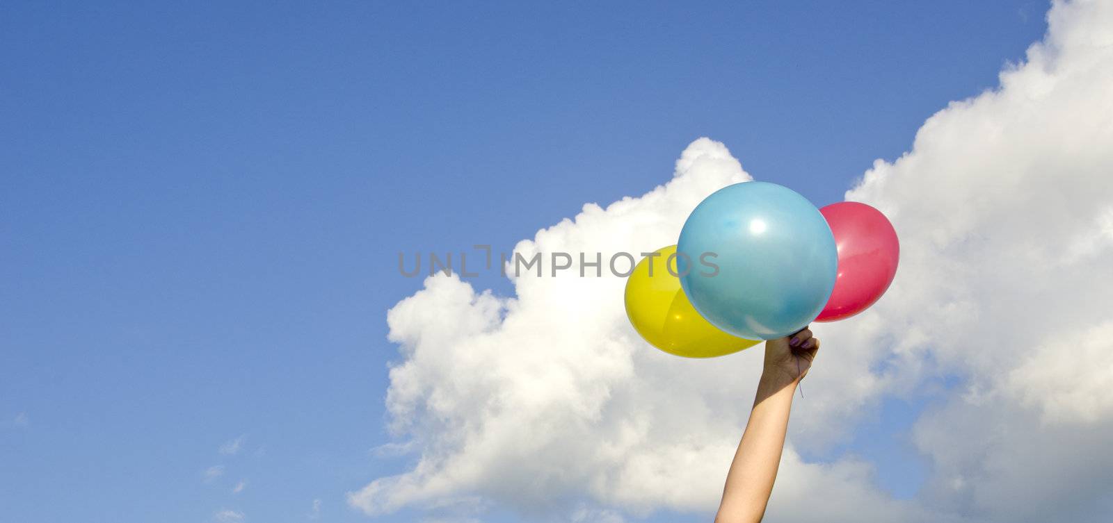 girls hand holding three colorful balloons and cloudy sky