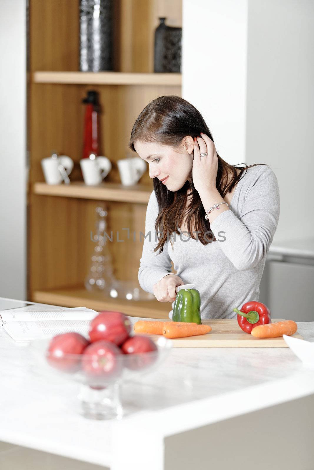 Beautiful young woman reading from a cookery book while cooking in her kitchen.