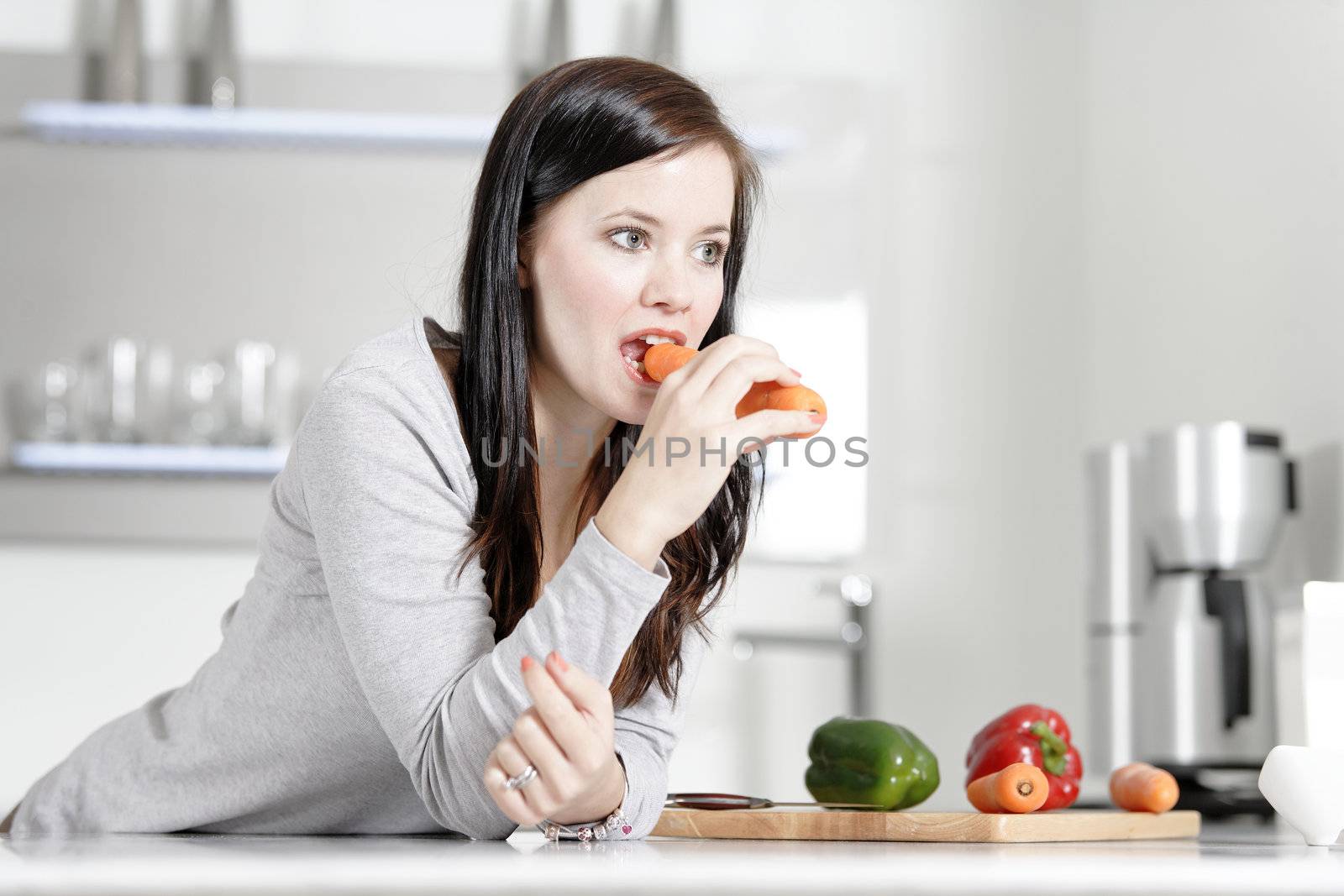 Attractive young woman in her elegant kitchen eating a raw carrot.