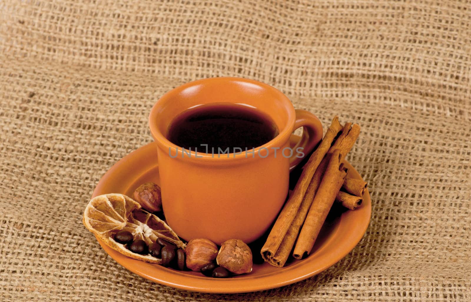 Closeup shot of freshly prepared cup of italian espresso with cinnamon, coffe beans, nuts and lemon over sacking