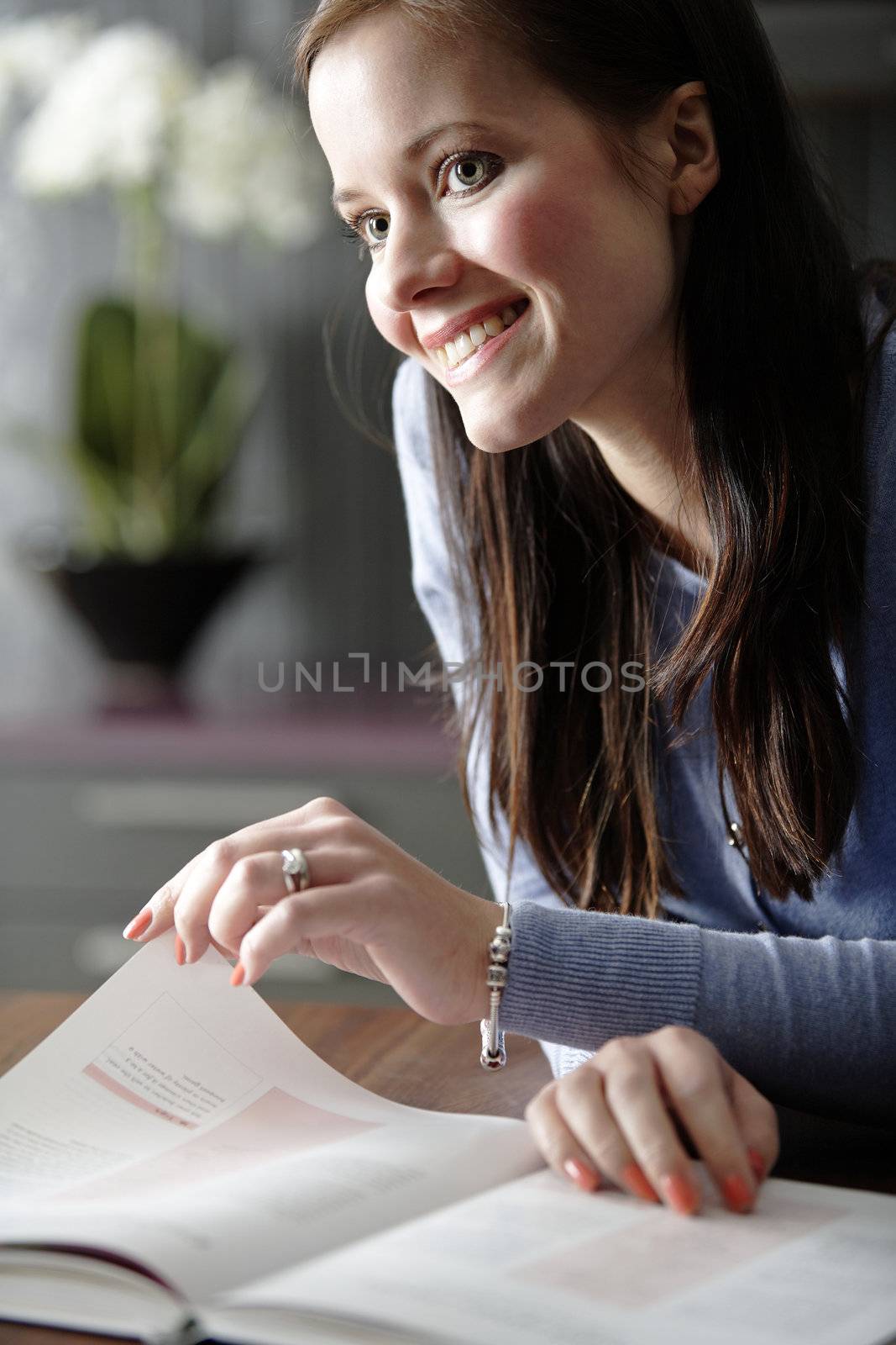 Attractive young woman reading a recipe from a cookery book in her kitchen.