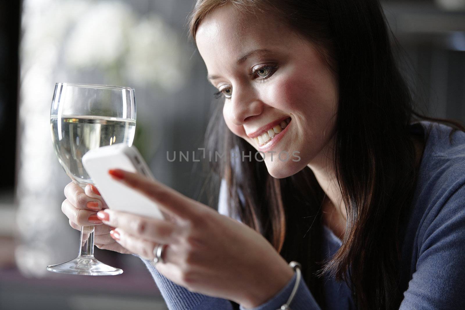 Attractive young woman enjoying a glass of wine in her kitchen while chatting on the phone.