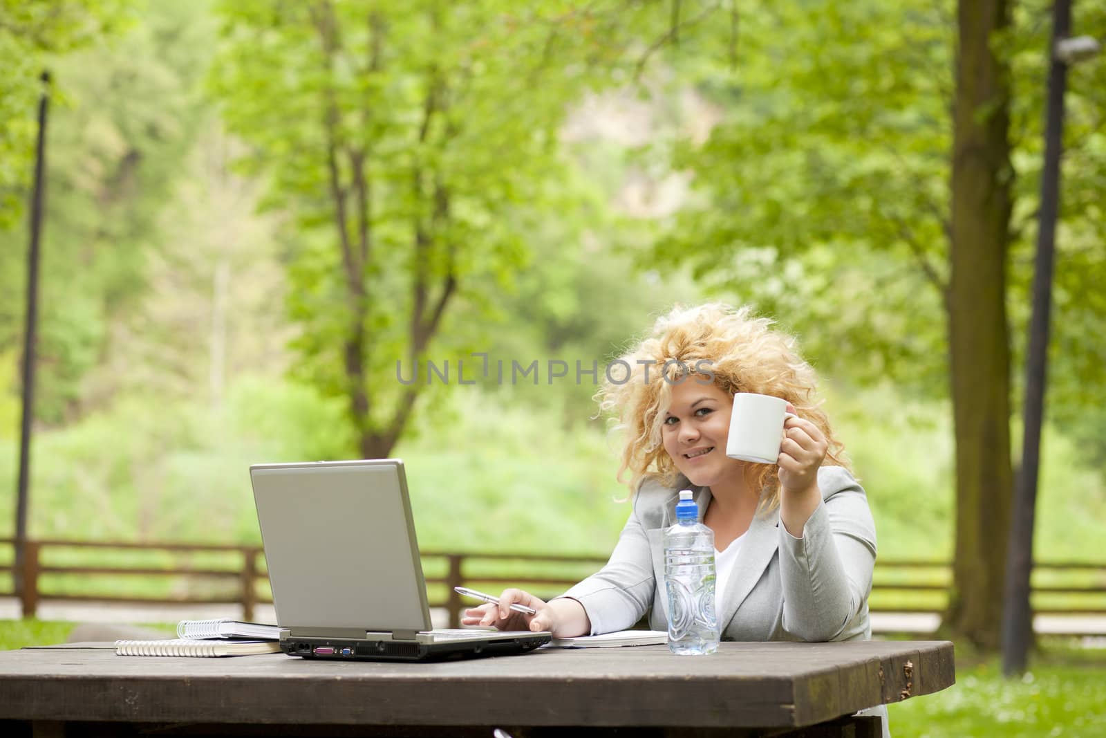 Woman using laptop in park and drinking by adamr