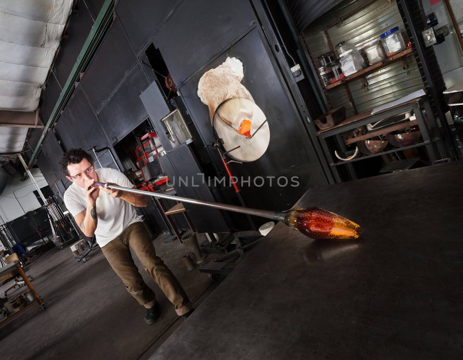 Glass artist with safety glasses and blowpipe forming a vase