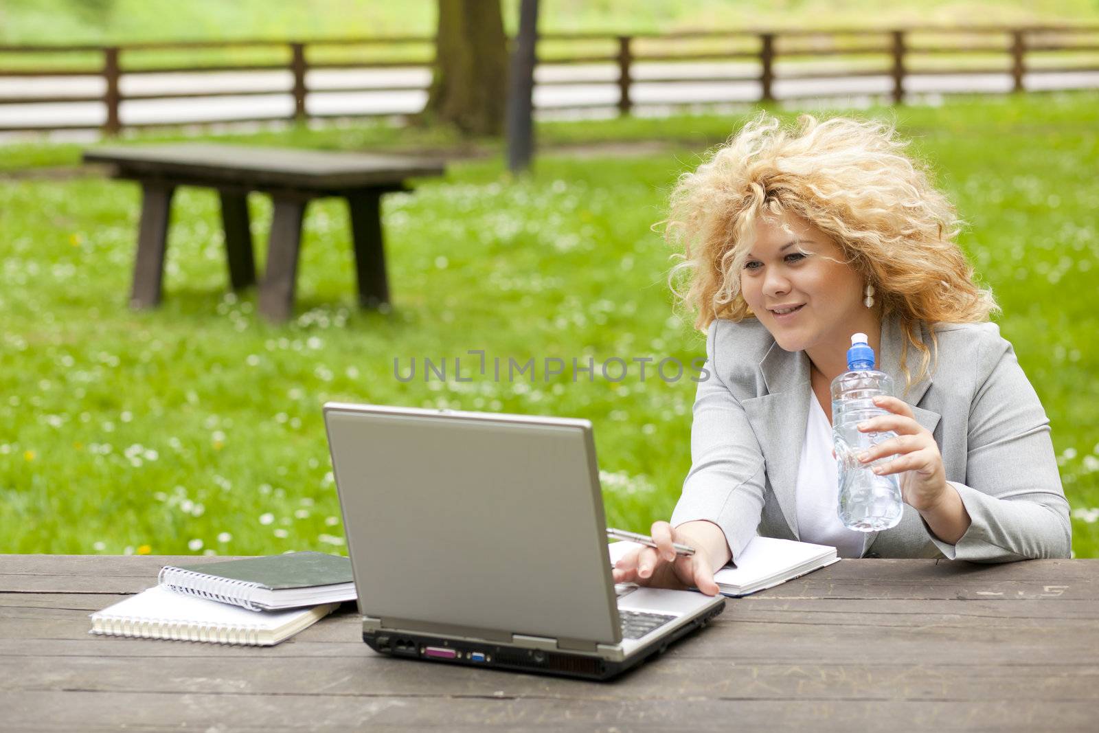 Young woman using laptop in park and drink water