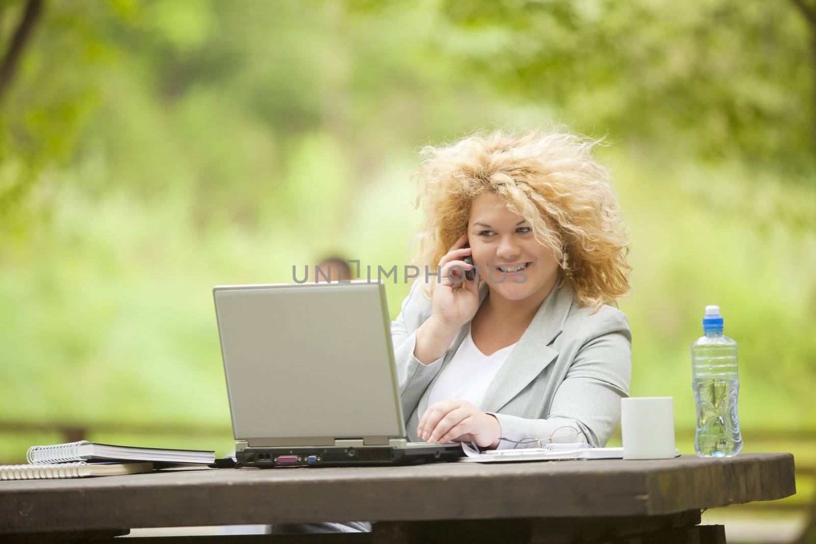 Young woman using laptop and phone in park