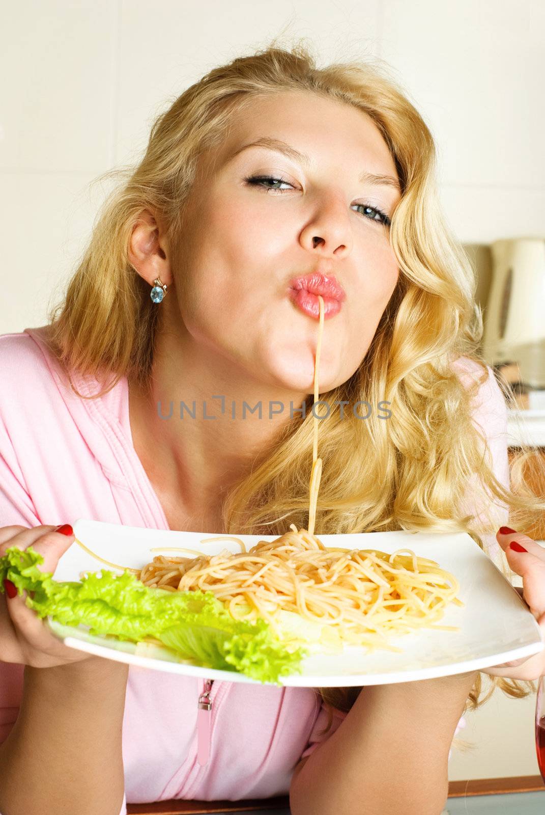 sexy blond woman at home in the kitchen eating spaghetti