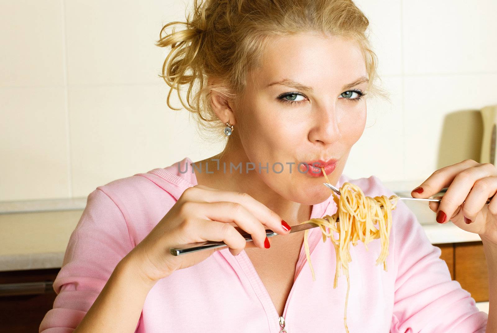 sexy young blond woman at home in the kitchen eating spaghetti