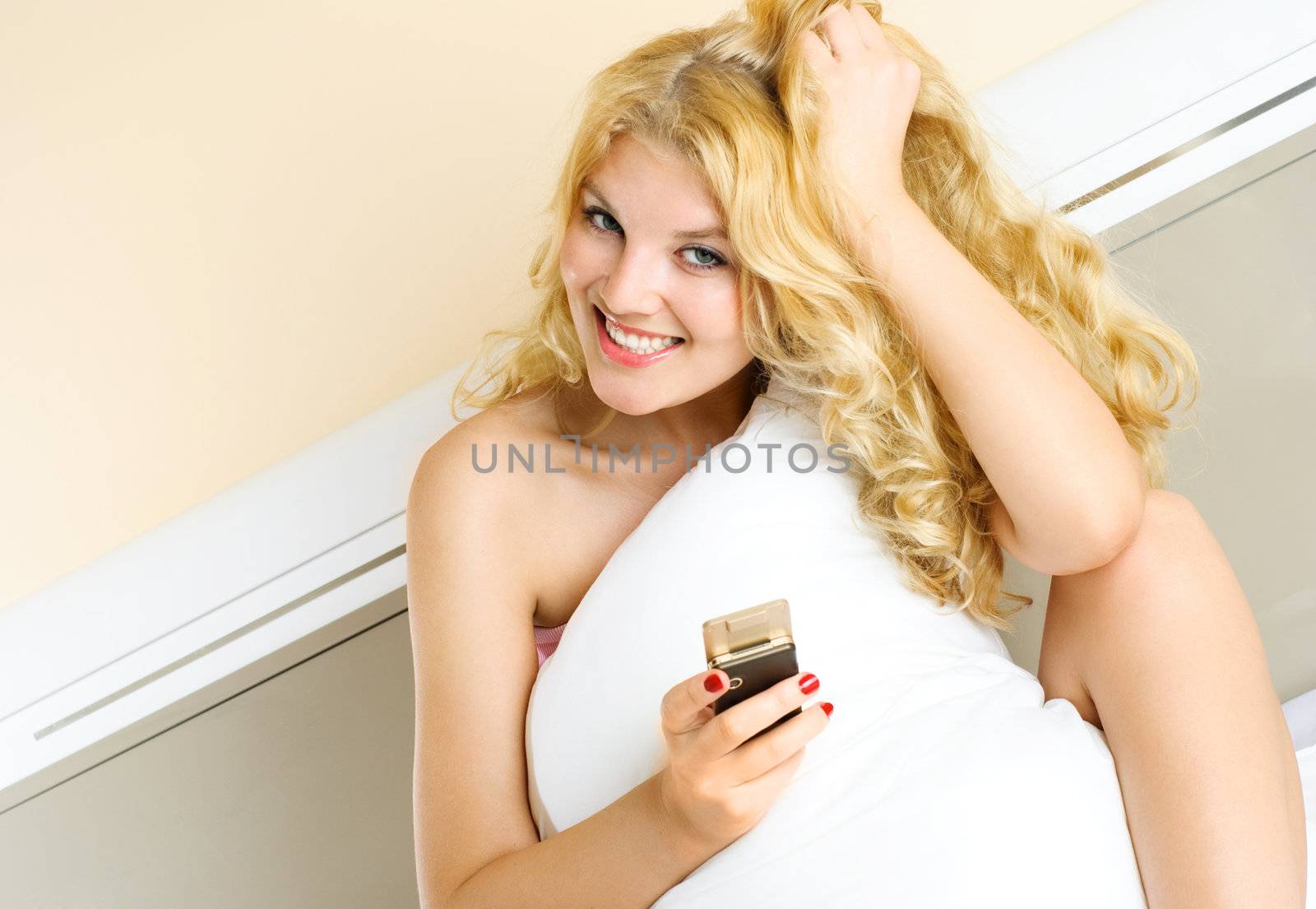 beautiful girl in her bed at home holding a cellphone in her hand