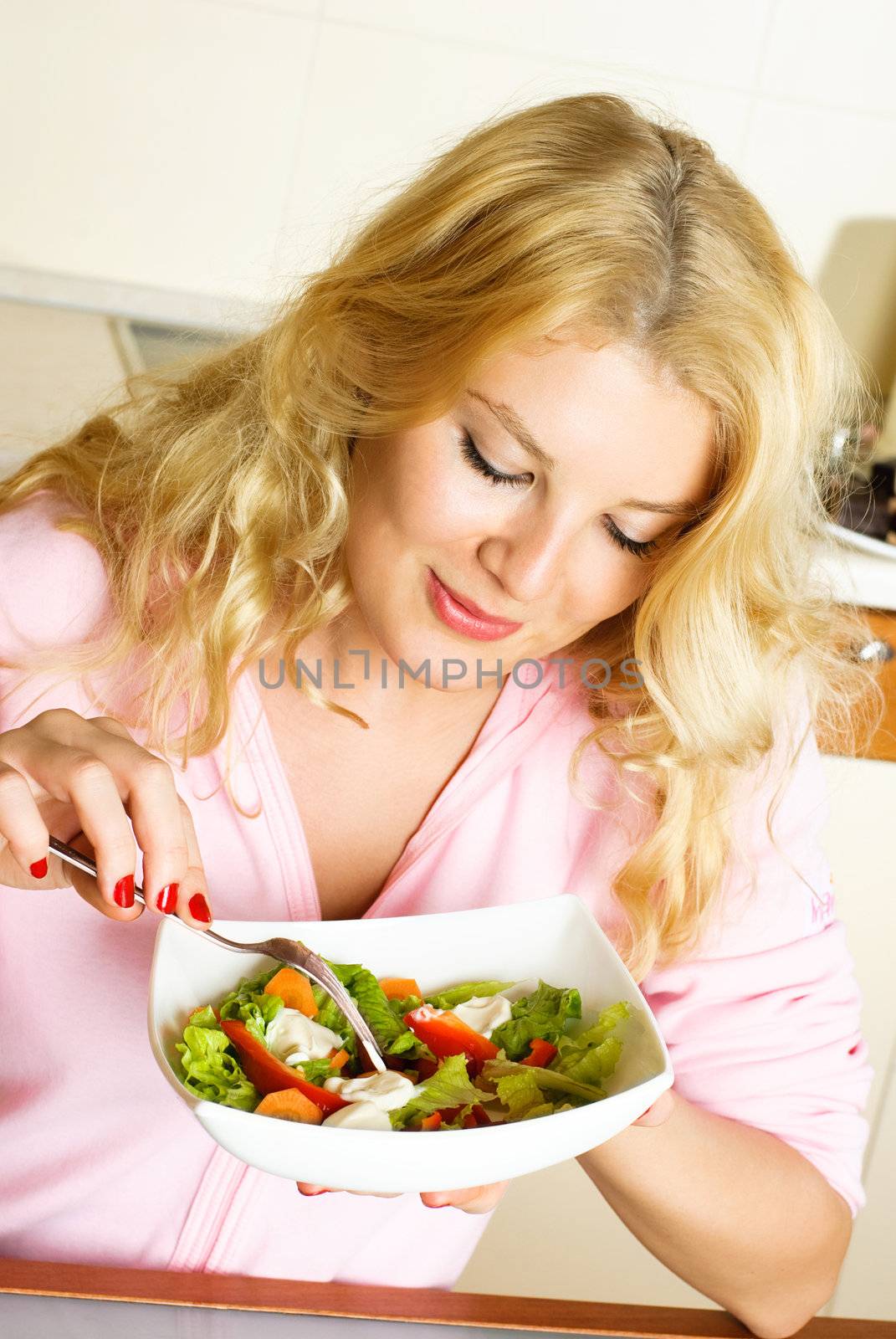 pretty young woman at home in the kitchen eating salad of vegetables