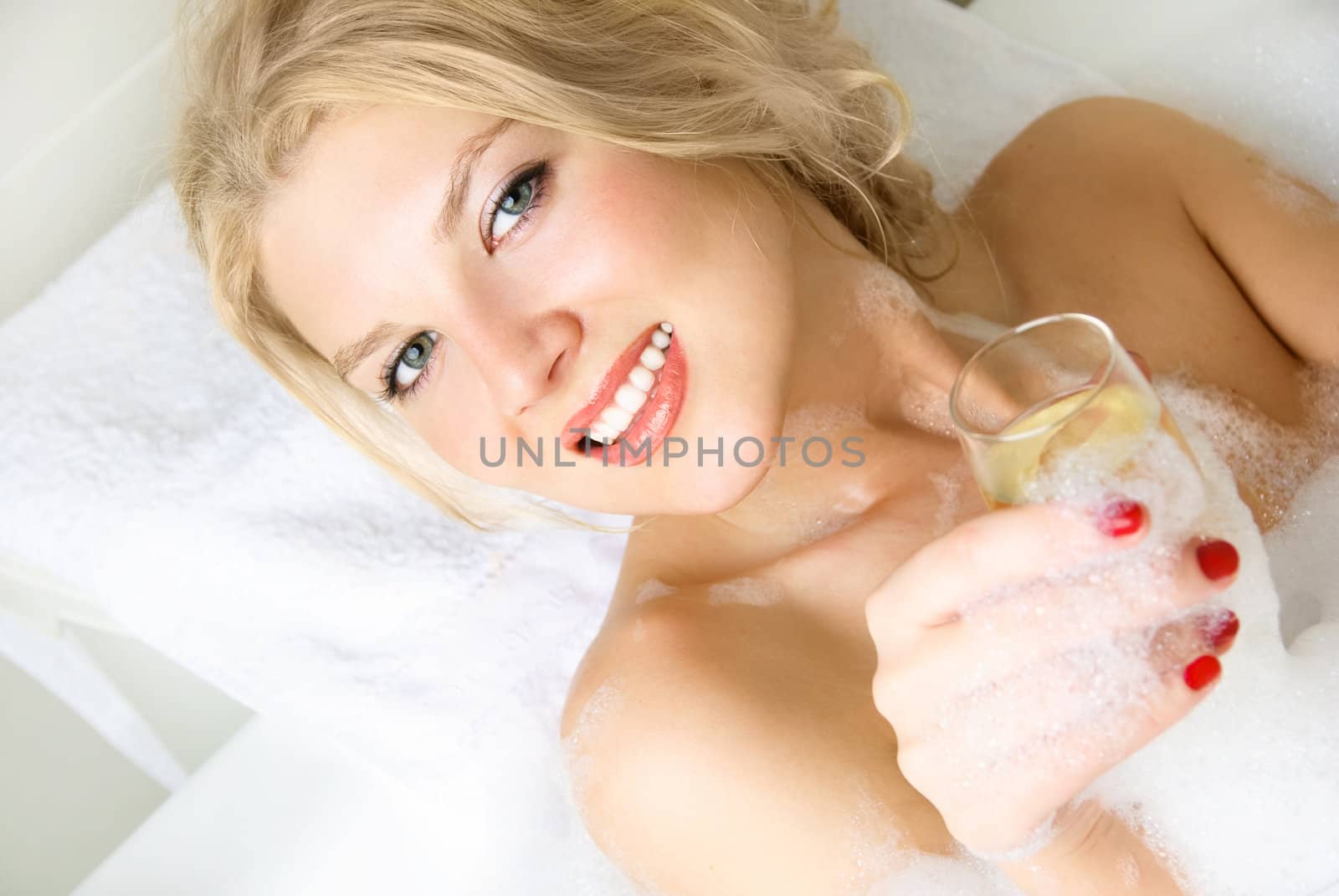 beautiful young blond woman relaxing in a bath with a glass of champagne