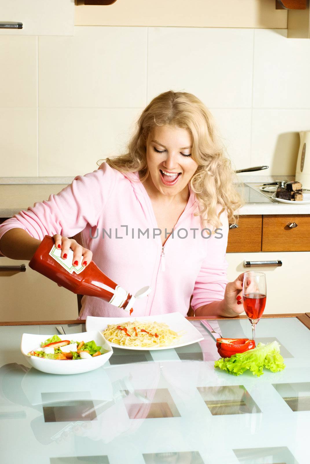 happy beautiful girl at home in the kitchen eating spaghetti and pouring ketchup 