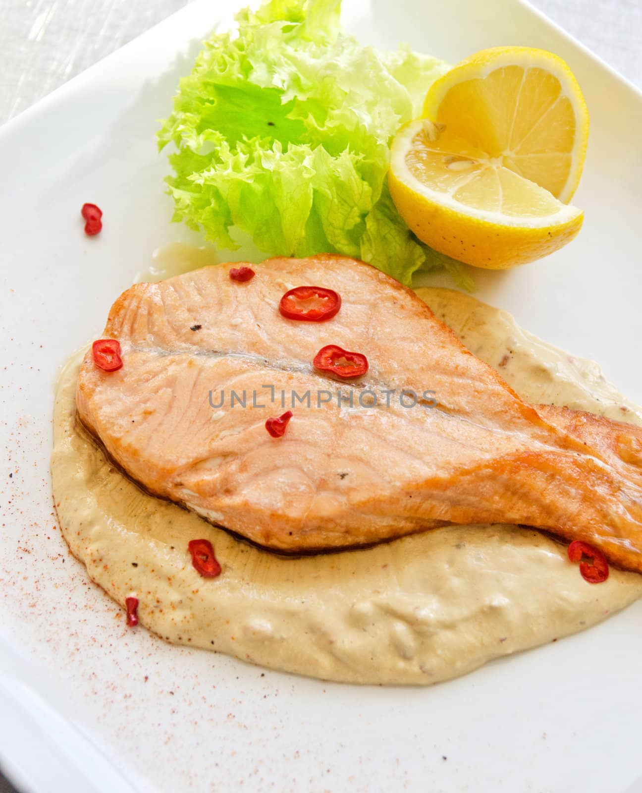Grilled salmon steak with greens, lemon, sauce and pepper chile