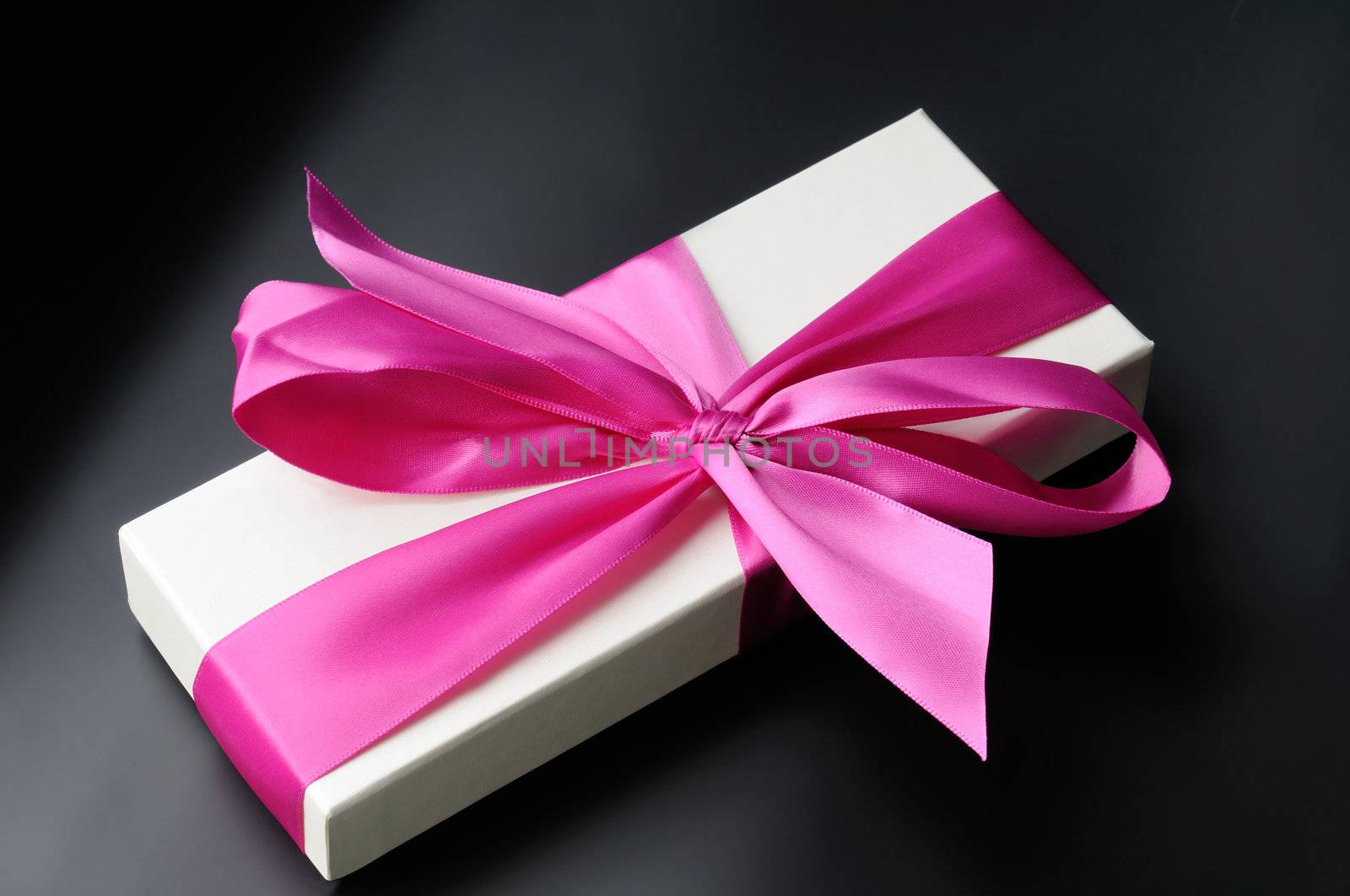 Gift box with a big pink bow. On a dark background.