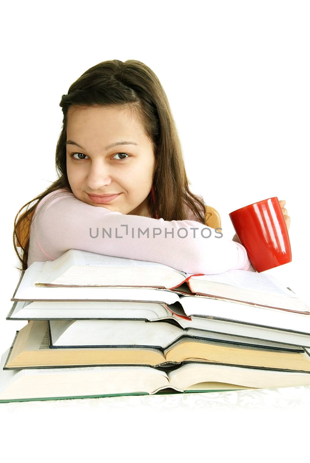 happy caucasian teenage girl sitting at the desk with stack of opened books and tea cup