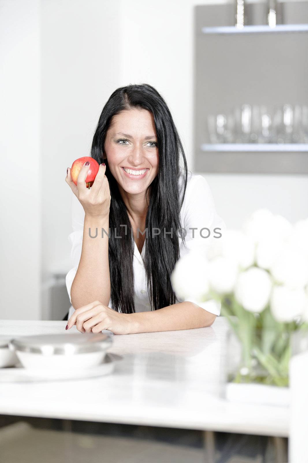 Beautiful young woman eating an apple in her kitchen at home