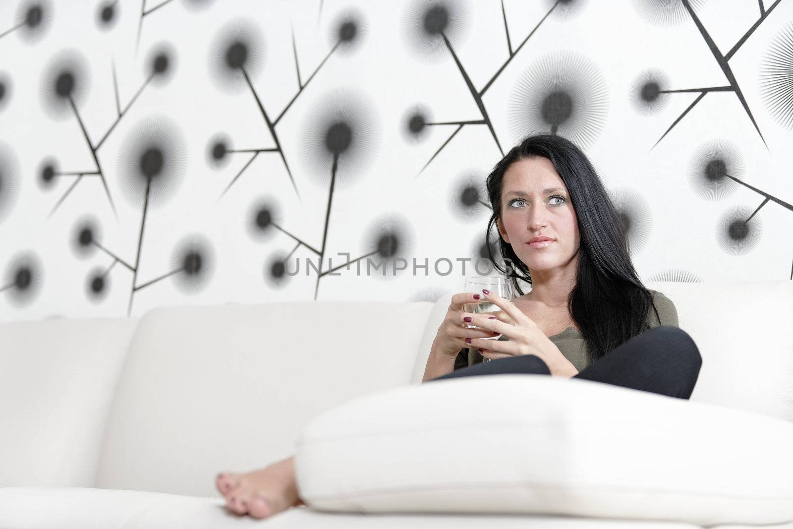 Attractive young woman relaxing on her sofa at home with a glass of white wine.