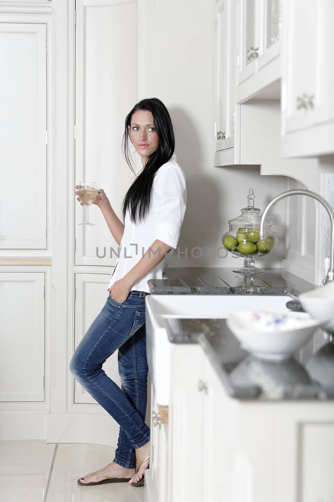 Attractive young woman enjoying a glass of wine in her kitchen.