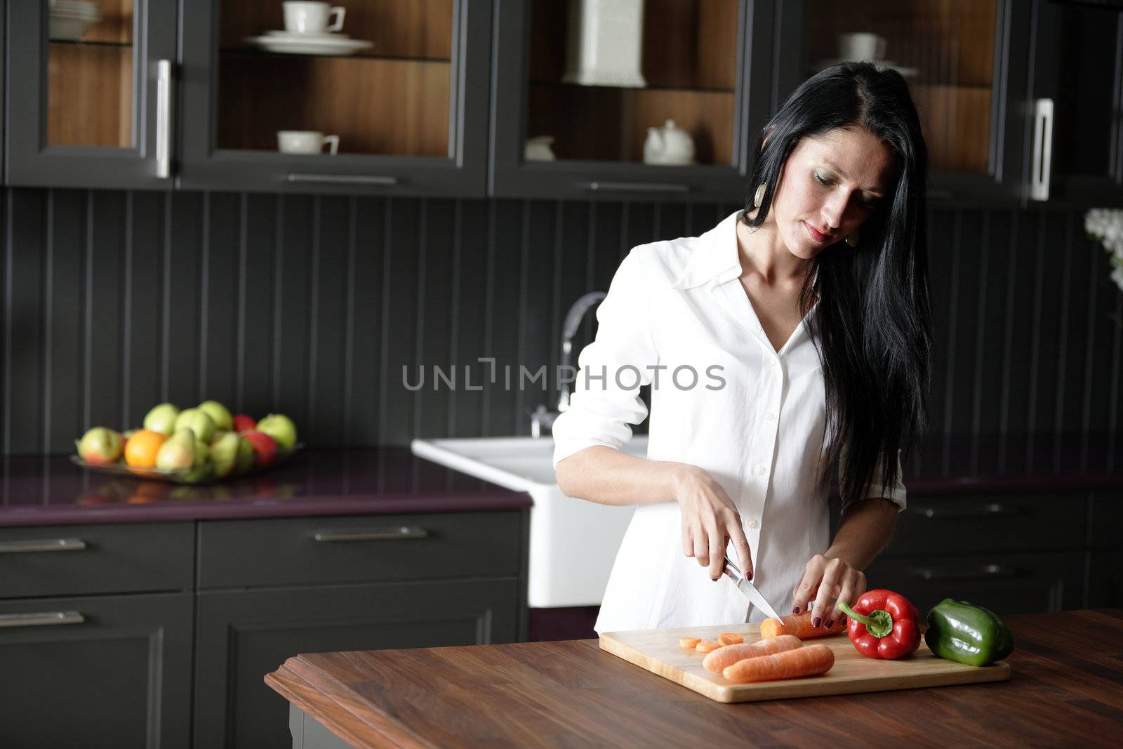 Attractive young woman chopping up fresh vegetables and peppers in her kitchen.