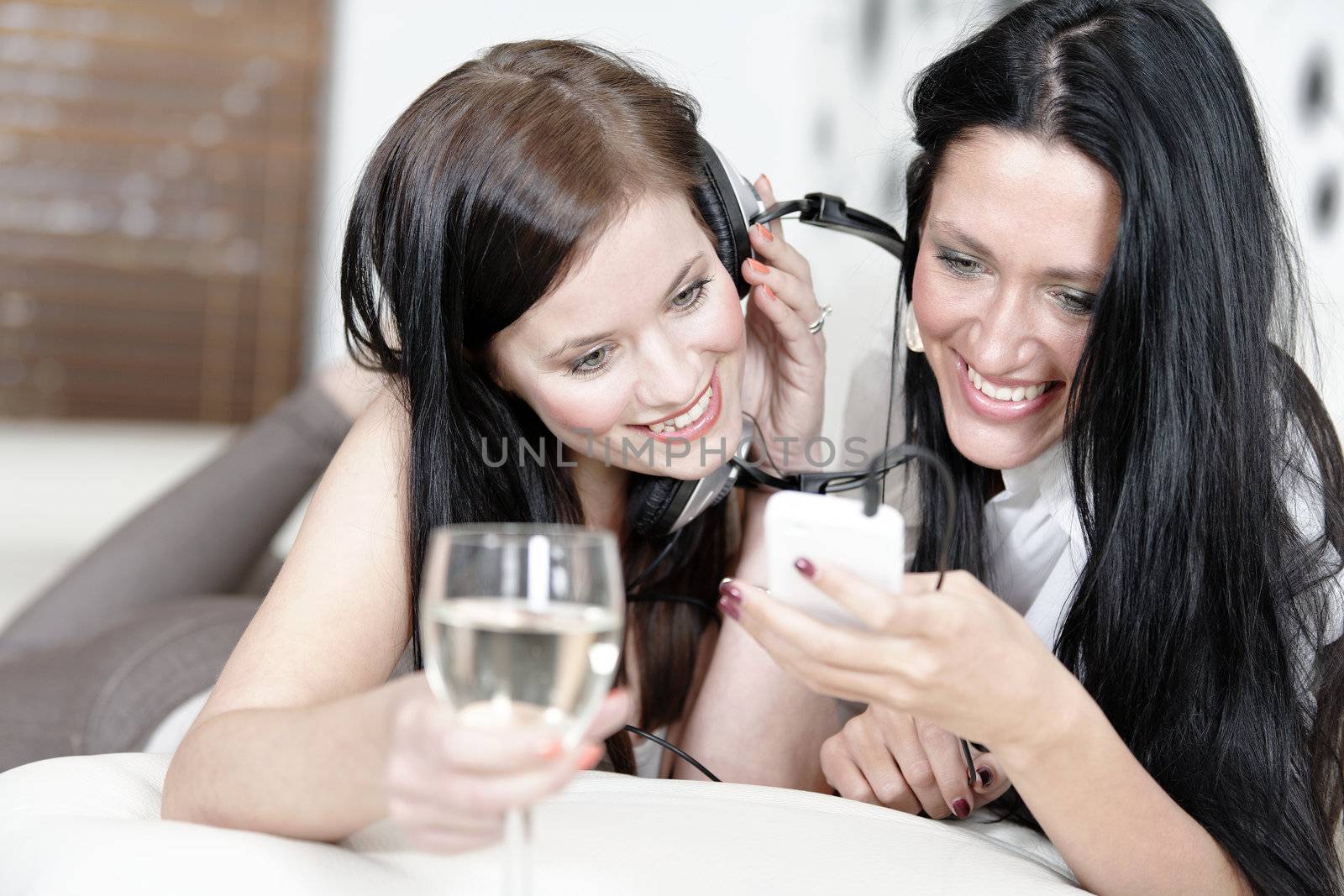 Two beautiful young woman listening to music on headphones at home on the sofa.