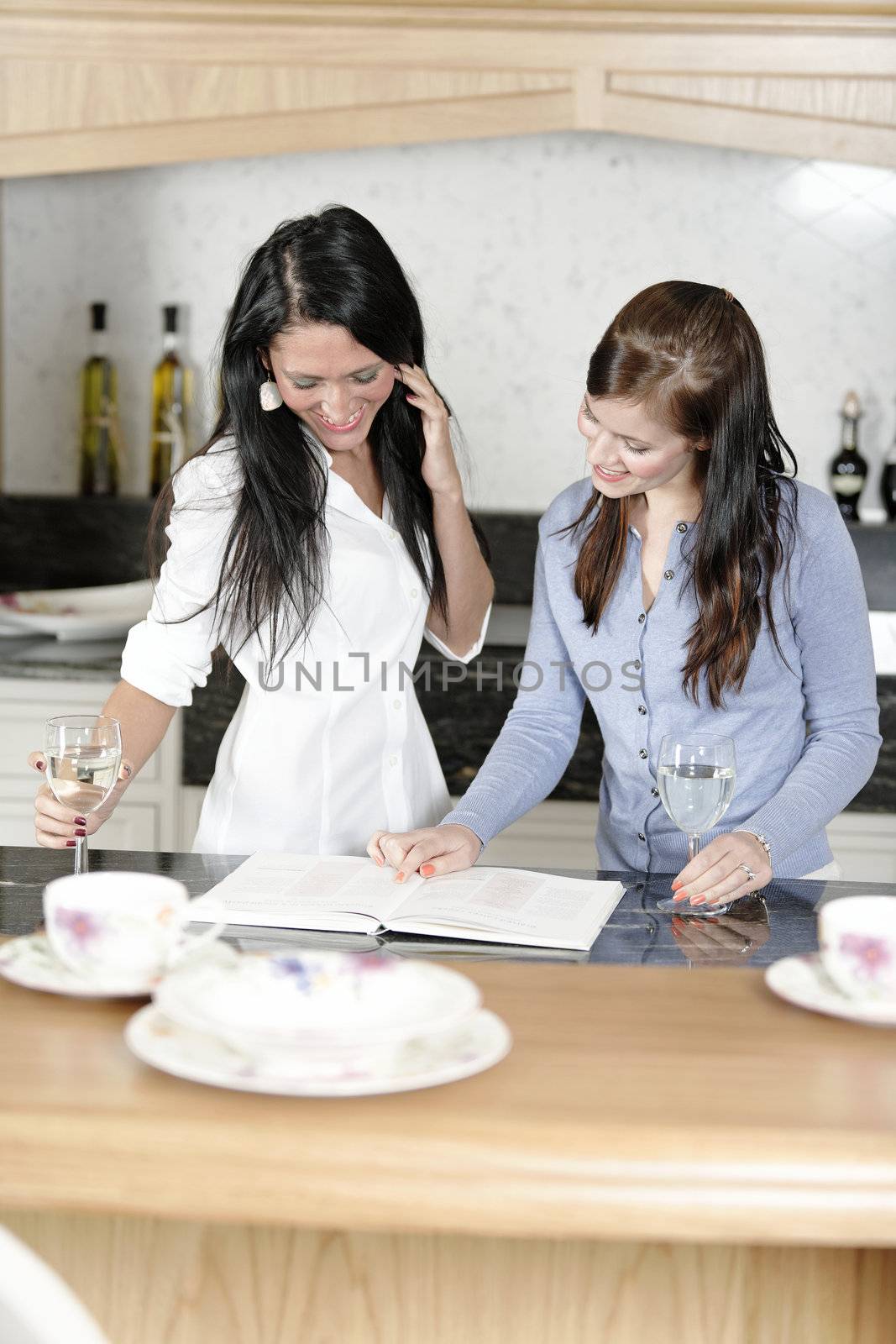 Two attractive friends looking at recipes in a cookery book in their kitchen.