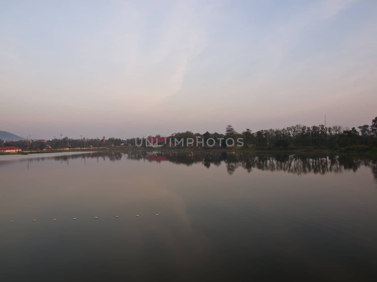 Morning breaks over the glassy still lake and tree background by gururugu