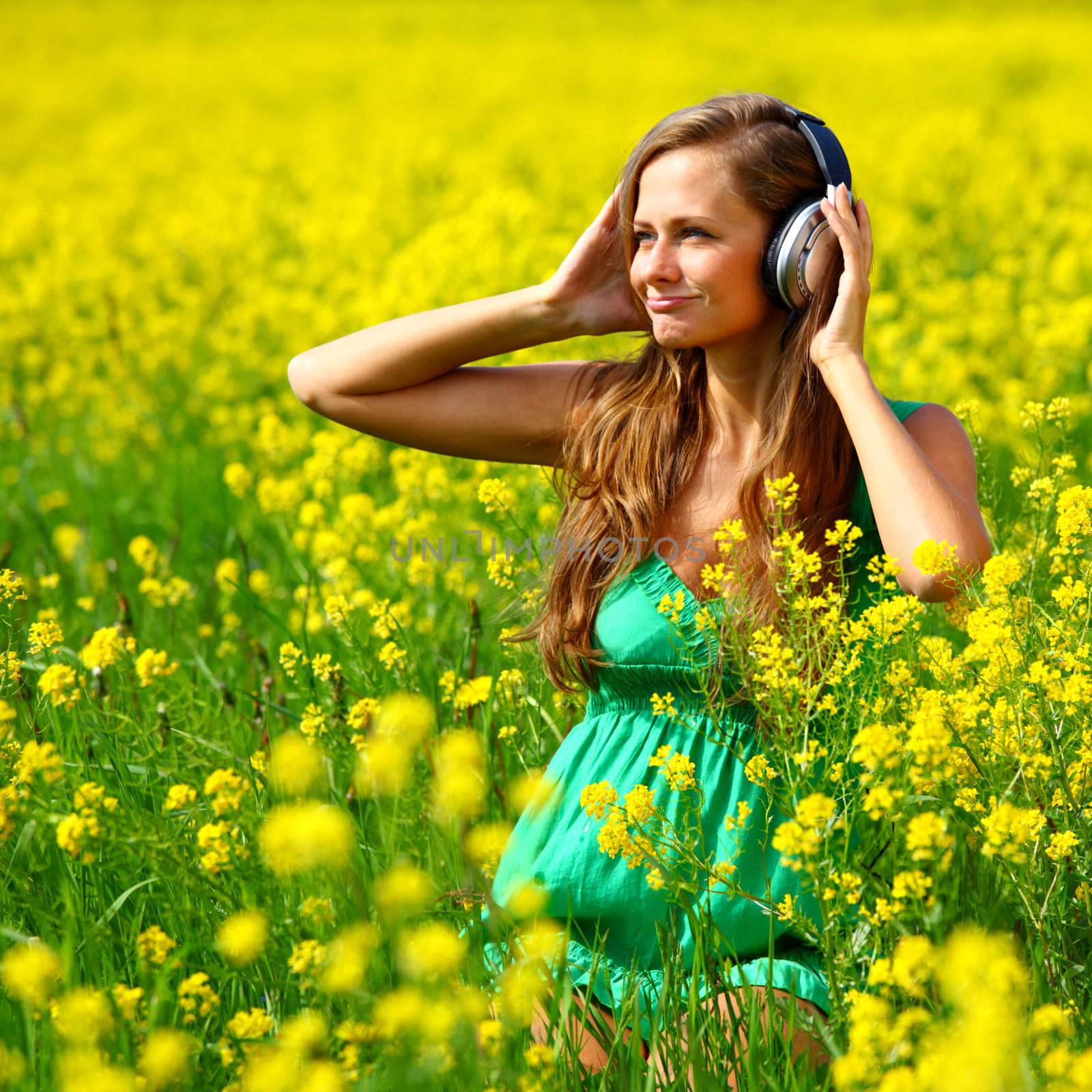  Young woman with headphones listening to music on oilseed flowering field
