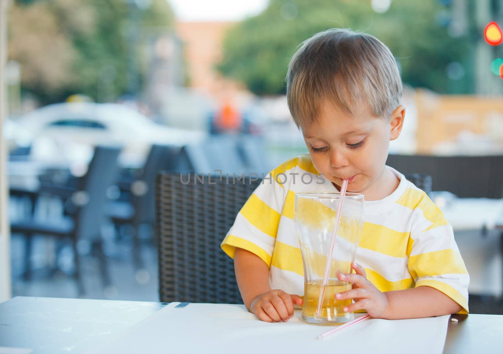 Casual portrait of adorable little boy drinking juice in outdoor restaurant