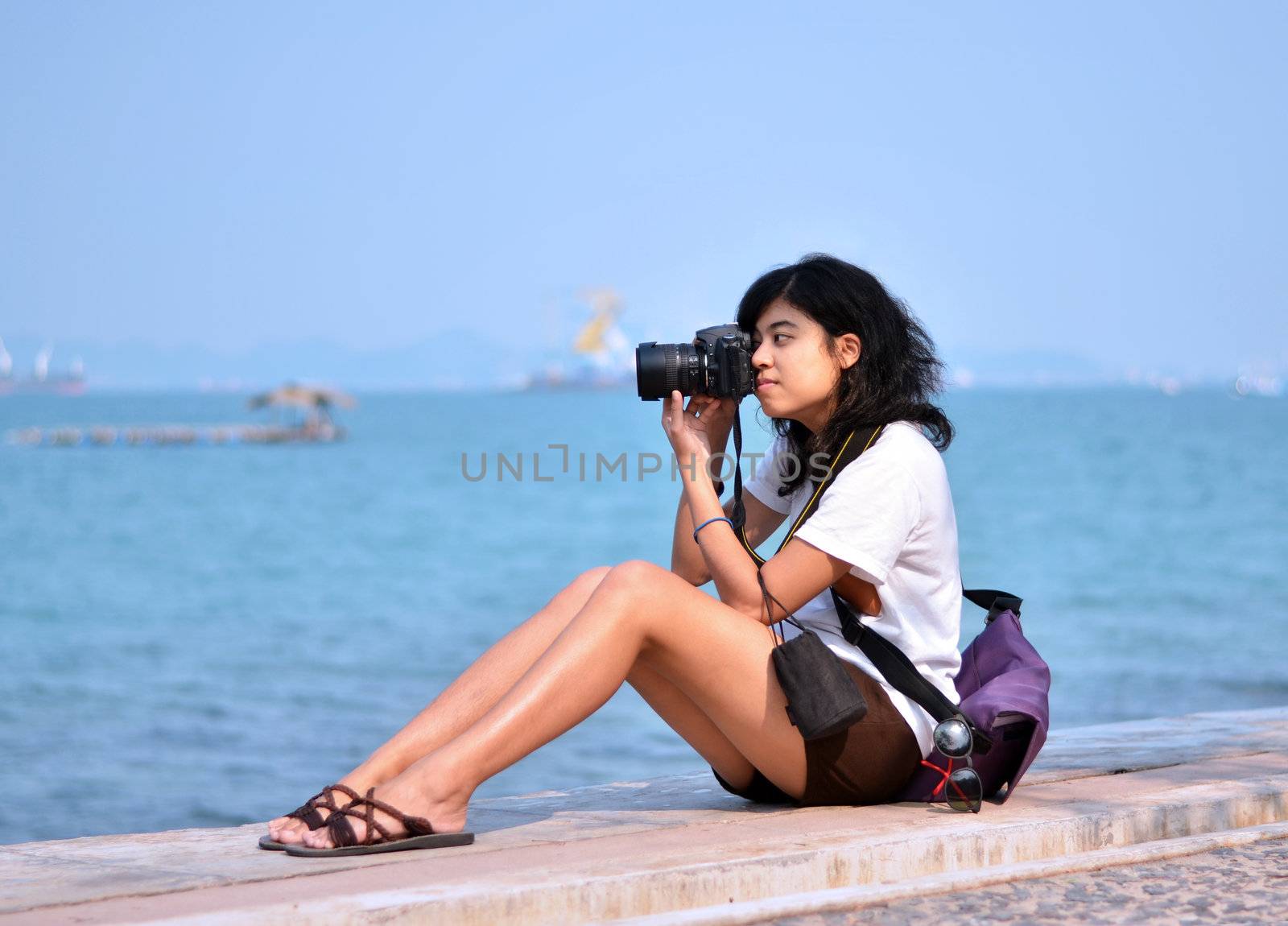 Beautiful young female photographer taking pictures on beach 