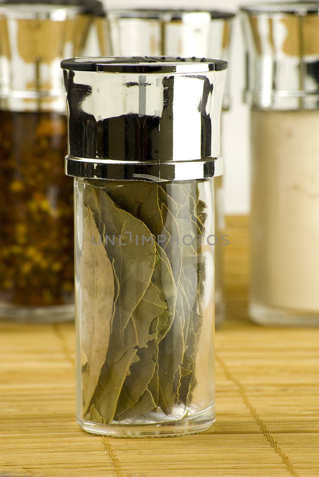 dry bay leaves in a glass jar on different spices background over wooden mat