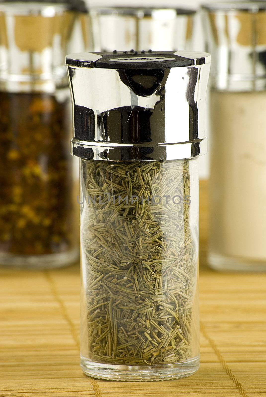 dry rosemary in a glass jar on different spices background over wooden mat