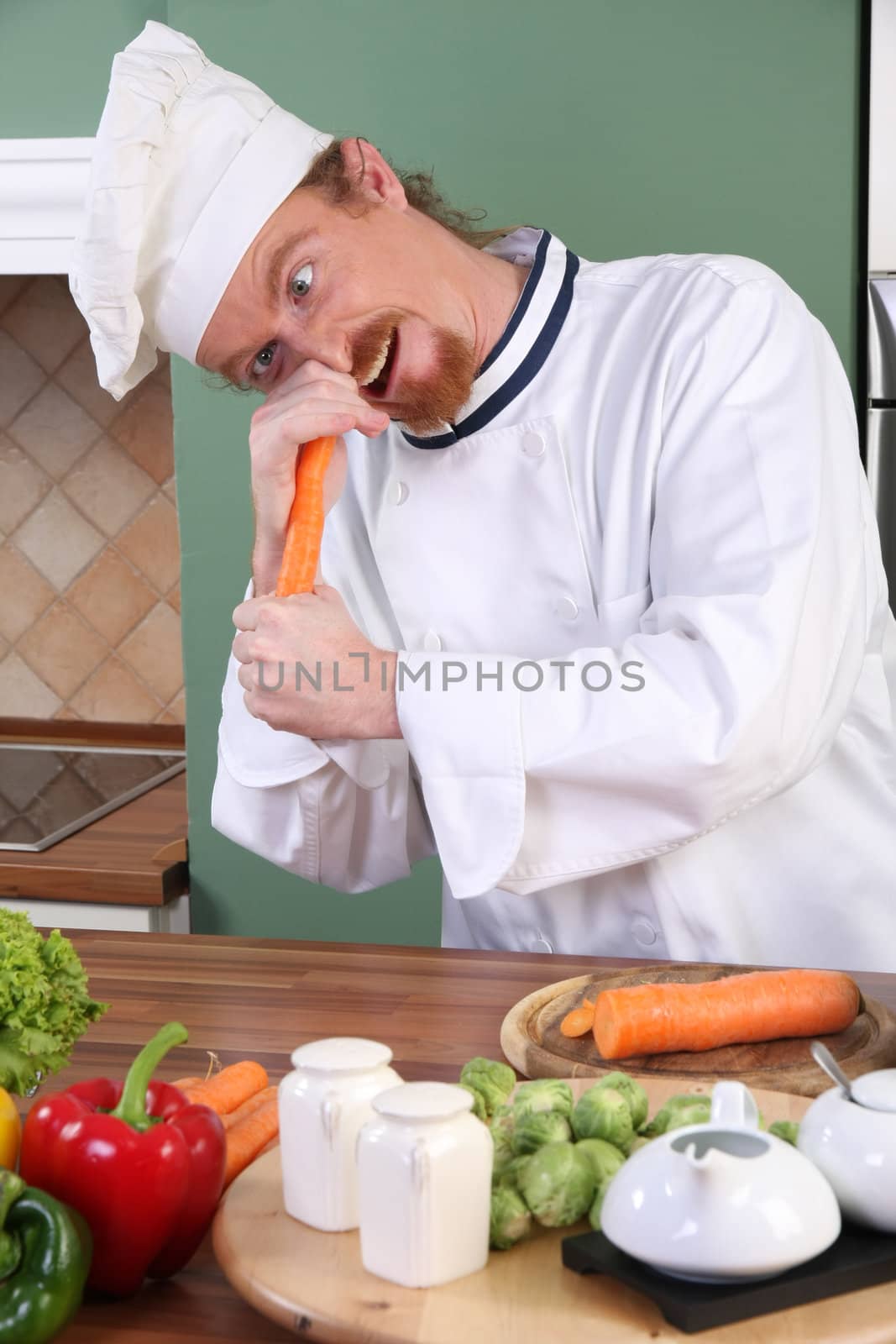 Funny young chef with carrot, preparing lunch in kitchen 