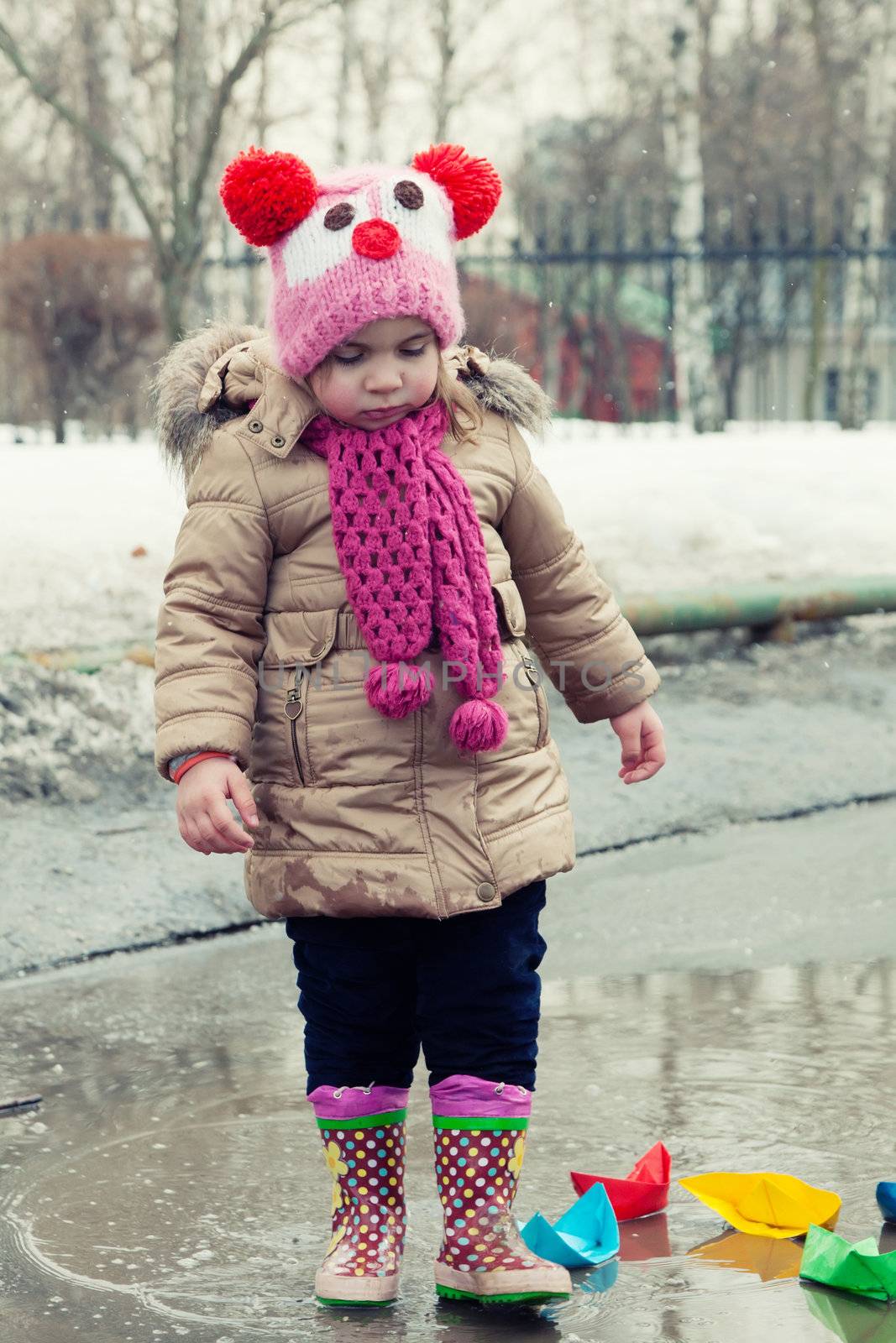 little girl plays with paper ships in a spring puddle