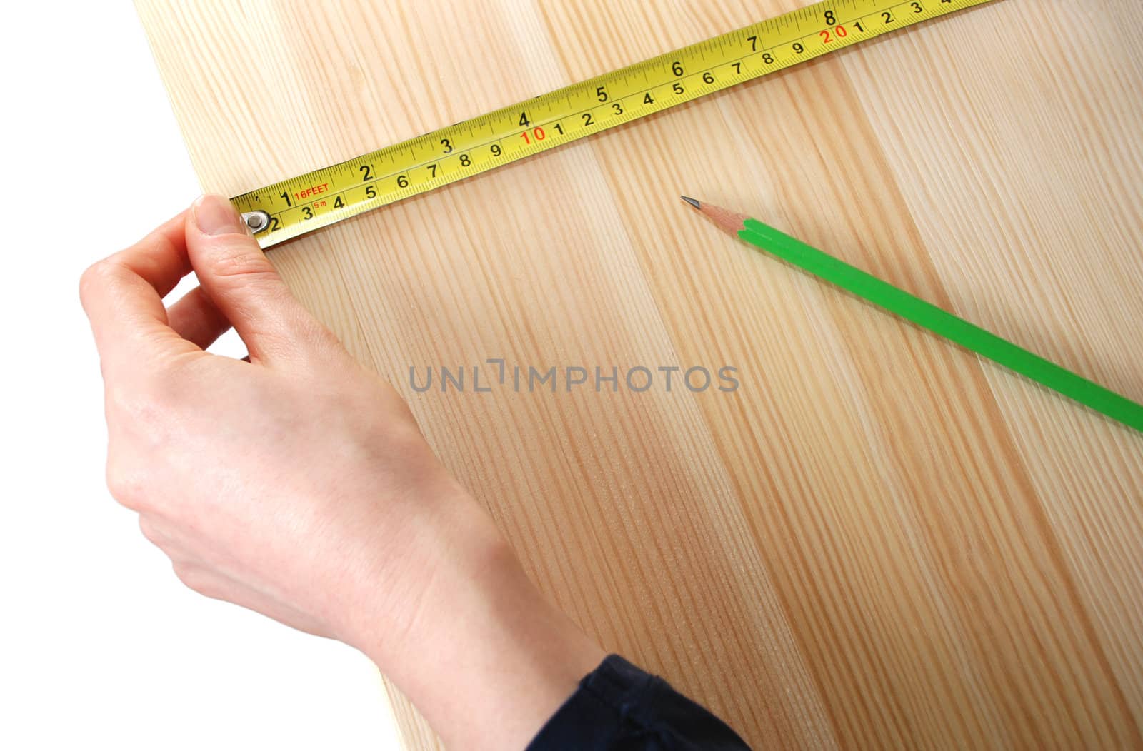 Closeup of hand holding a steel tape measure on a wooden board against a white background