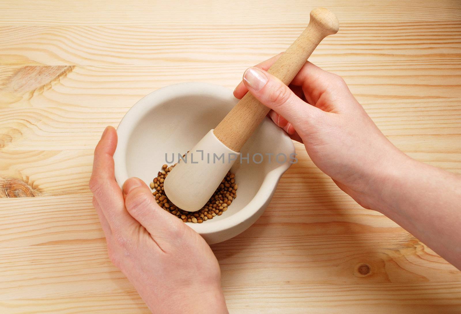 A woman uses a pestle and mortar on a wooden table to crush whole coriander seeds