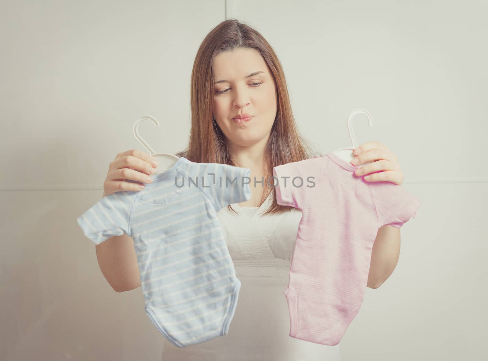 Pregnant woman holding bodysuits  for a girl or a boy in soft pa by doble.d