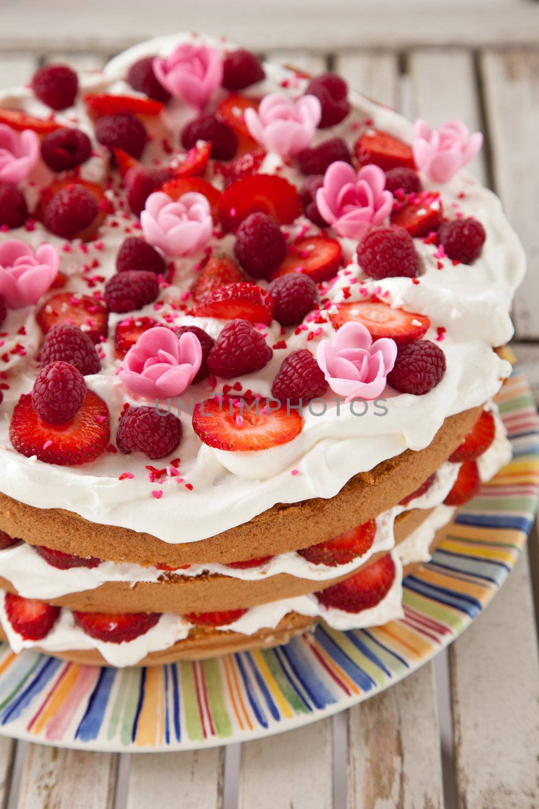 Delicious layered birthday cake dressed with fruit, whipped cream and marzipan flowers