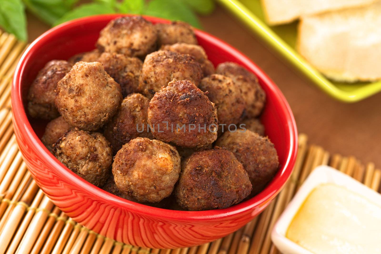 Meatball appetizers in a bowl with sauce and baguette slices (Selective Focus, Focus on the meatball in the middle of the image)