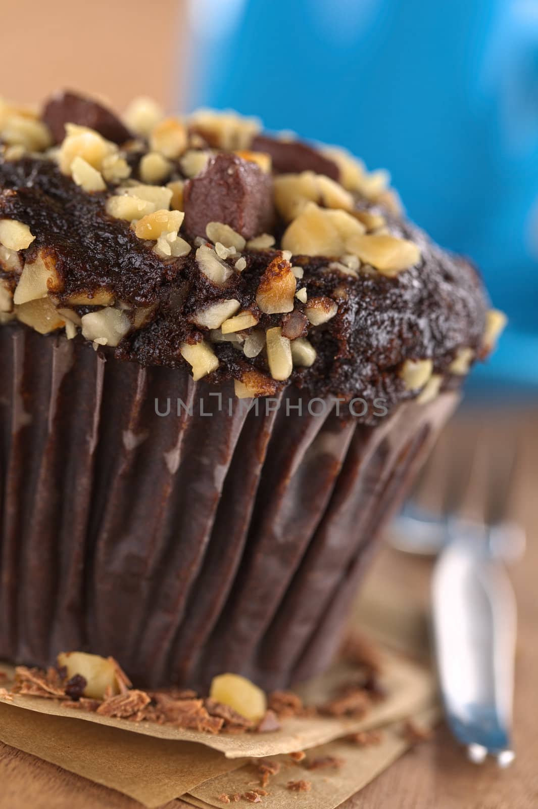 Chocolate-walnut muffin with coffee cup in the back (Selective Focus, Focus on the front edge of the muffin) 