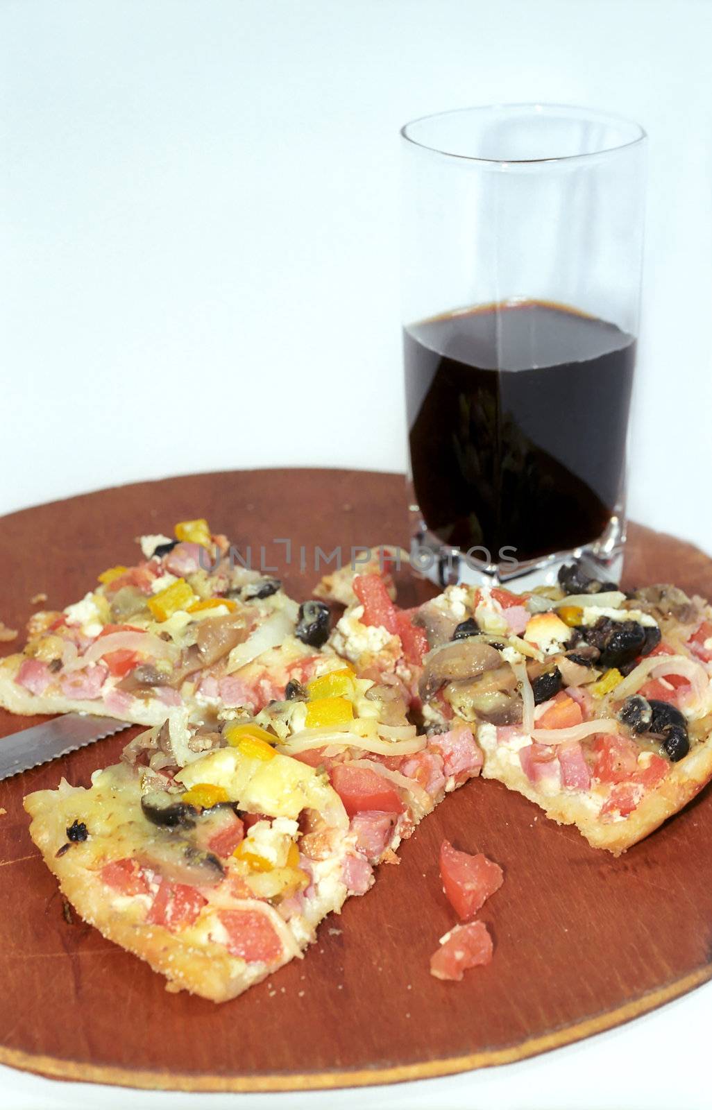 Parts of cutting pizza with ham and vegetables and dark drink glass 