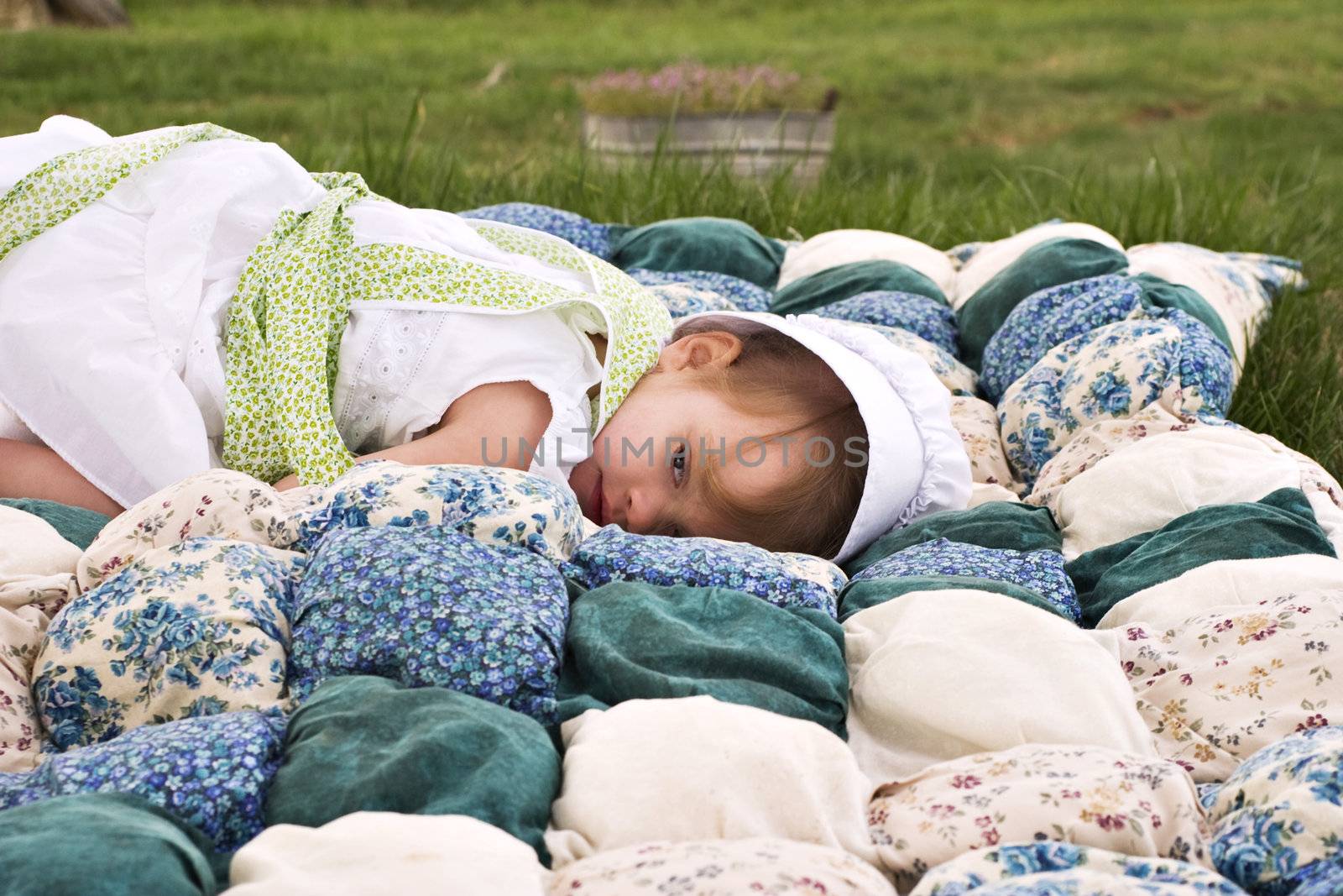 Amish child lying outdoors on a handmade biscuit quilt.