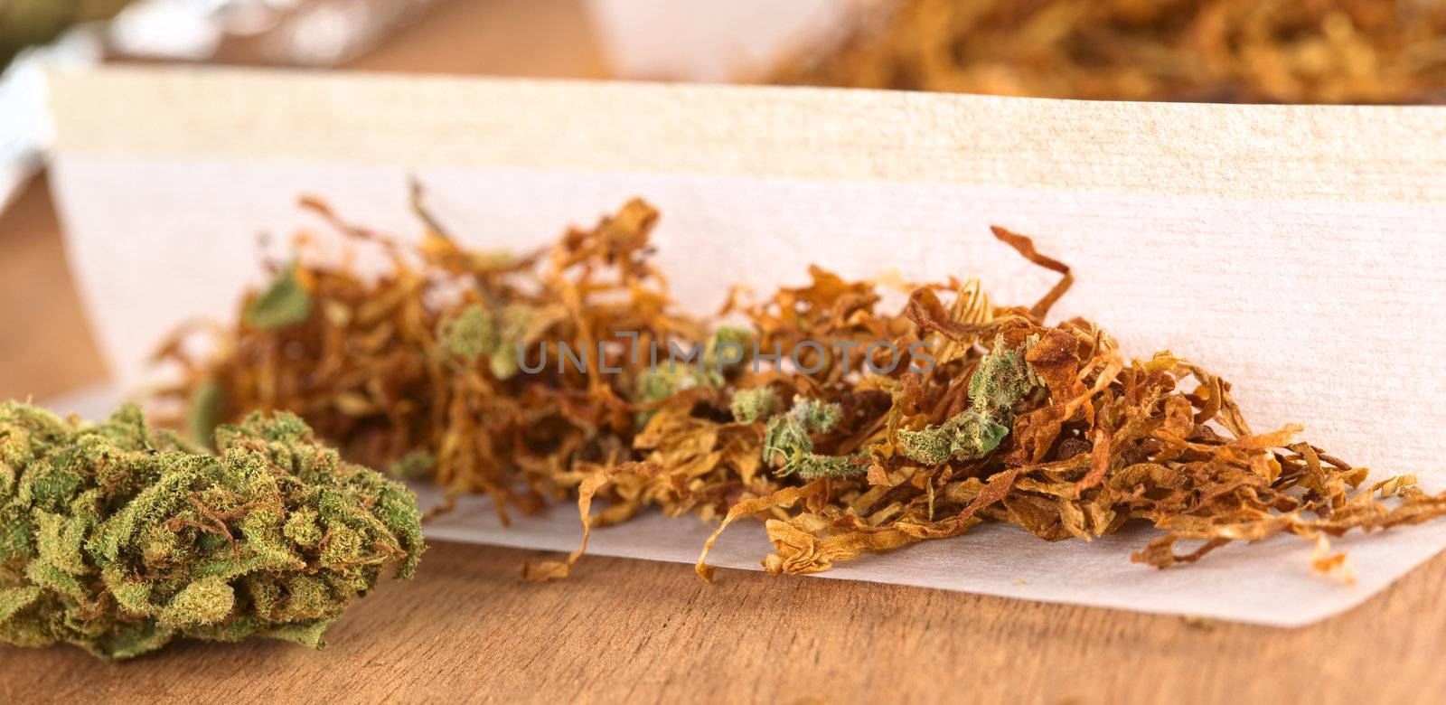 Rolling a joint out of marijuana and tobacco (Selective Focus, Focus on the front of the marijuana flower on the left and on the marijuana in the joint on the right)