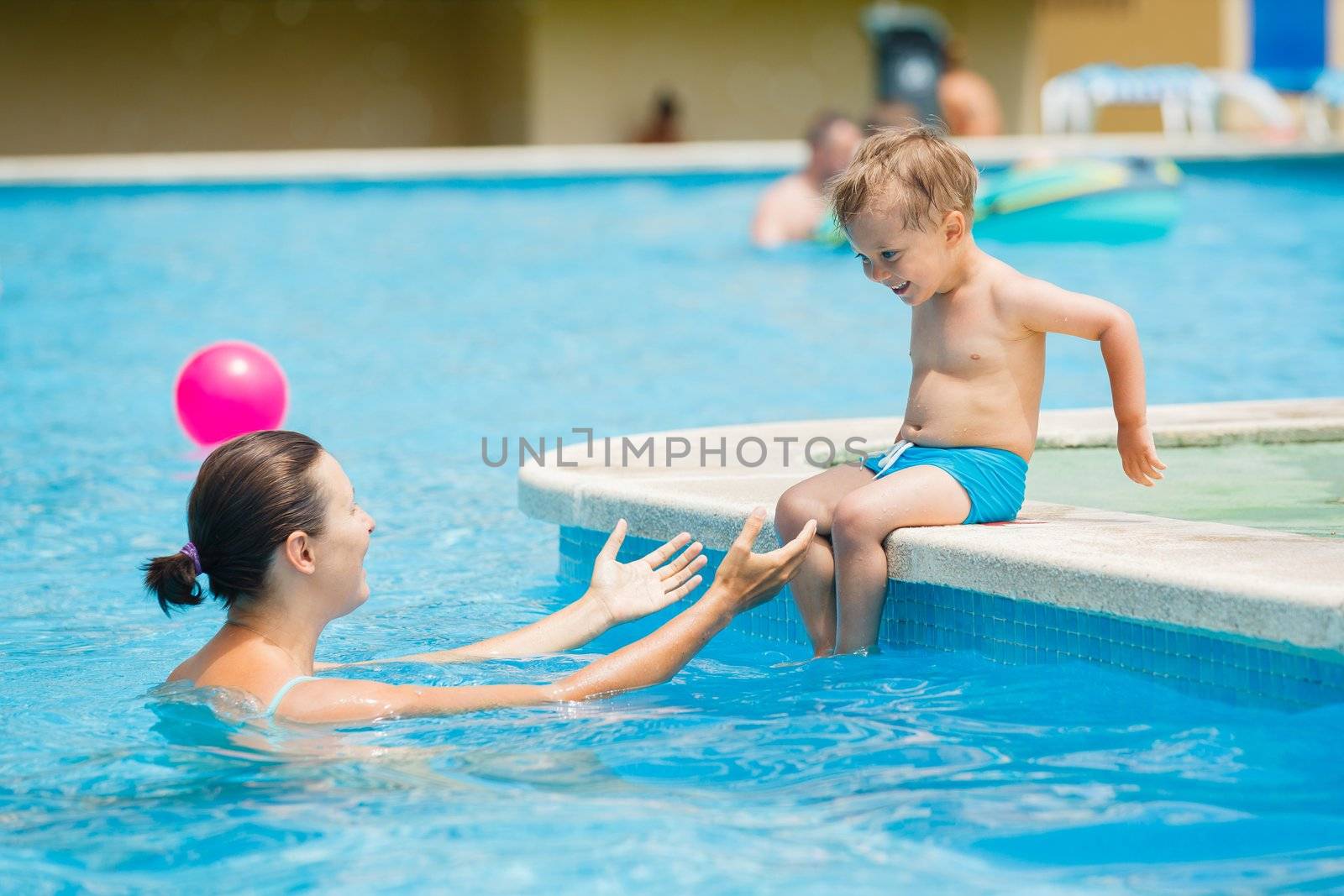 Cute boy with his mother playing in a pool of water during the summer