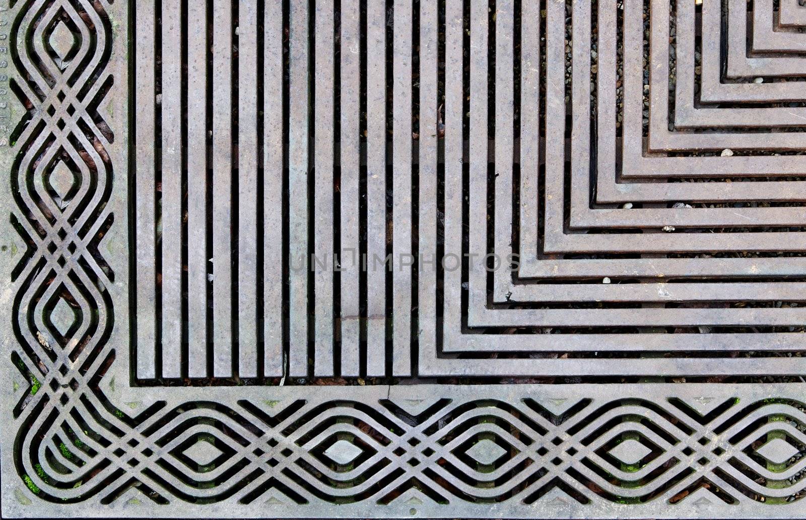 Corner of an ornately designed steek grating on the sidewalk