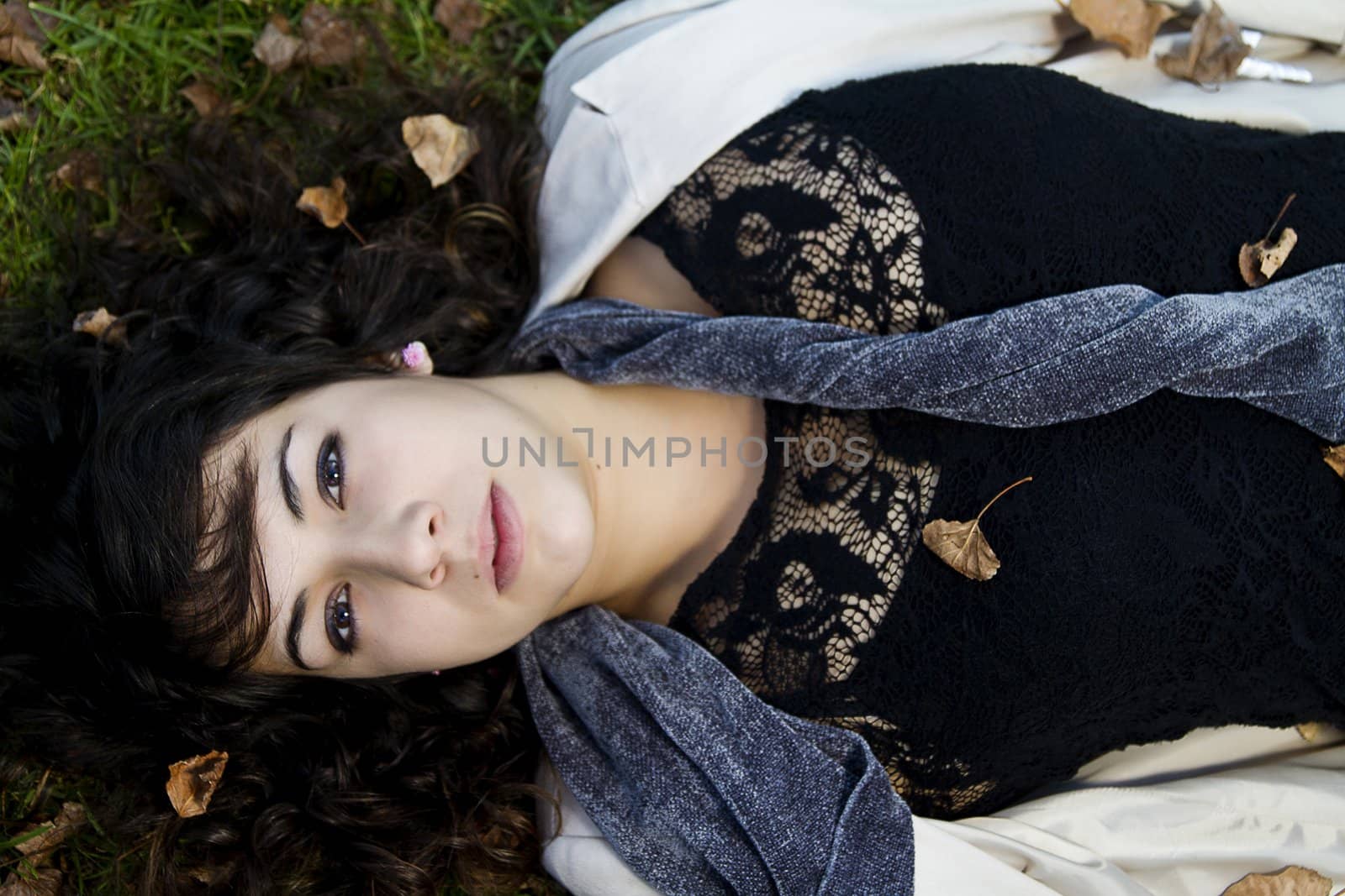 Beautiful young girl lies down on the green grass with fallen leaves.