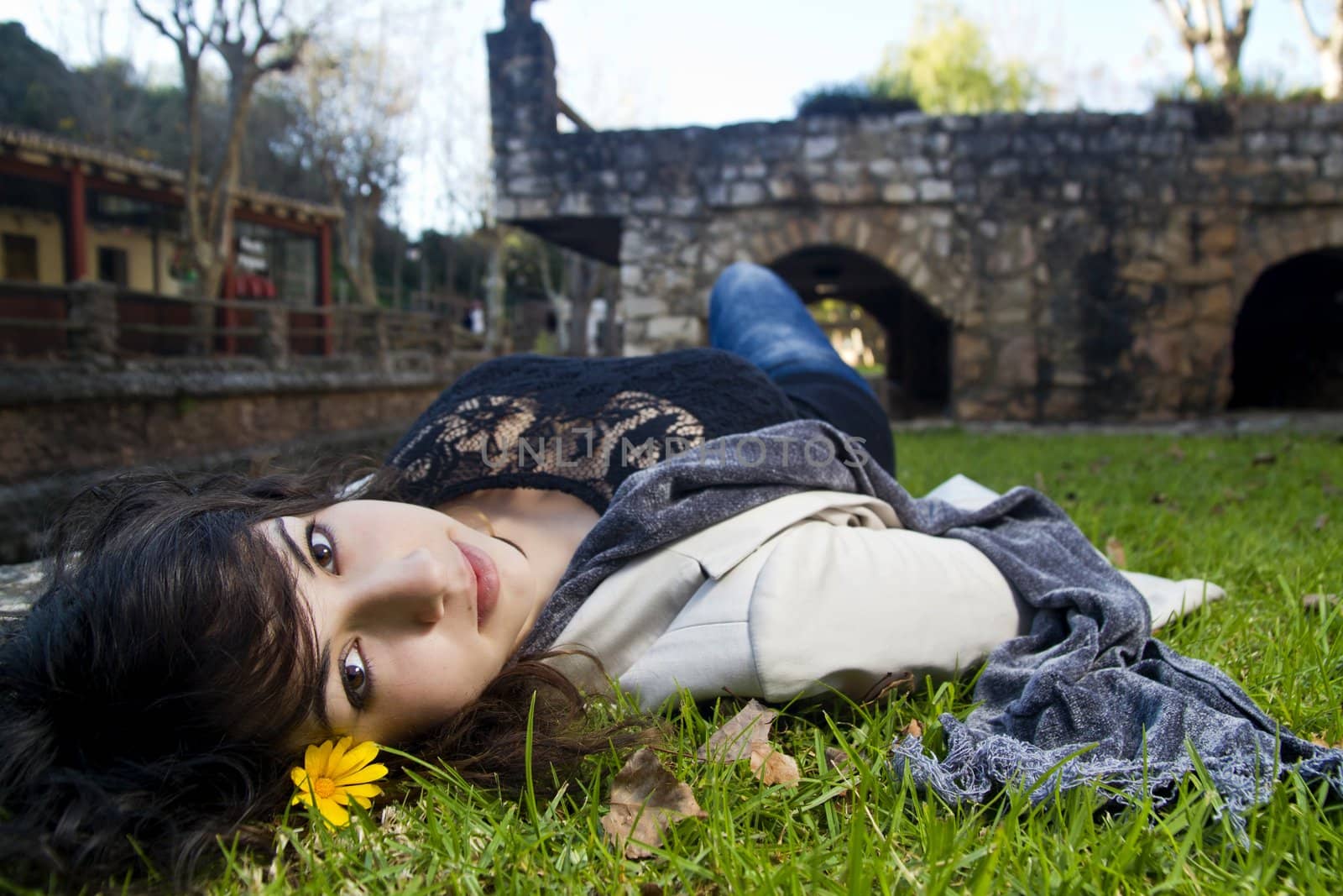 Beautiful young girl lies down on the green grass on a urban park.