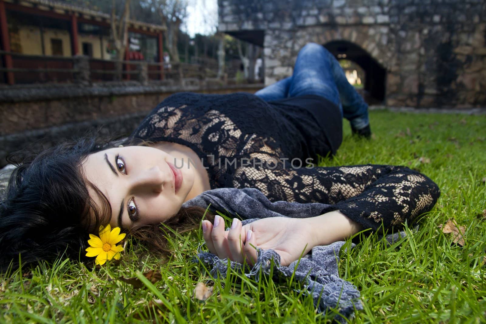 Beautiful young girl lies down on the green grass on a urban park.