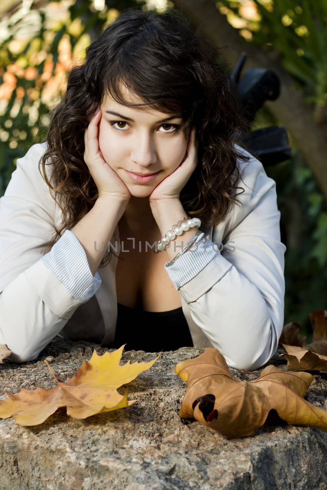 Beautiful young girl lies down on a stone rock on a urban park.